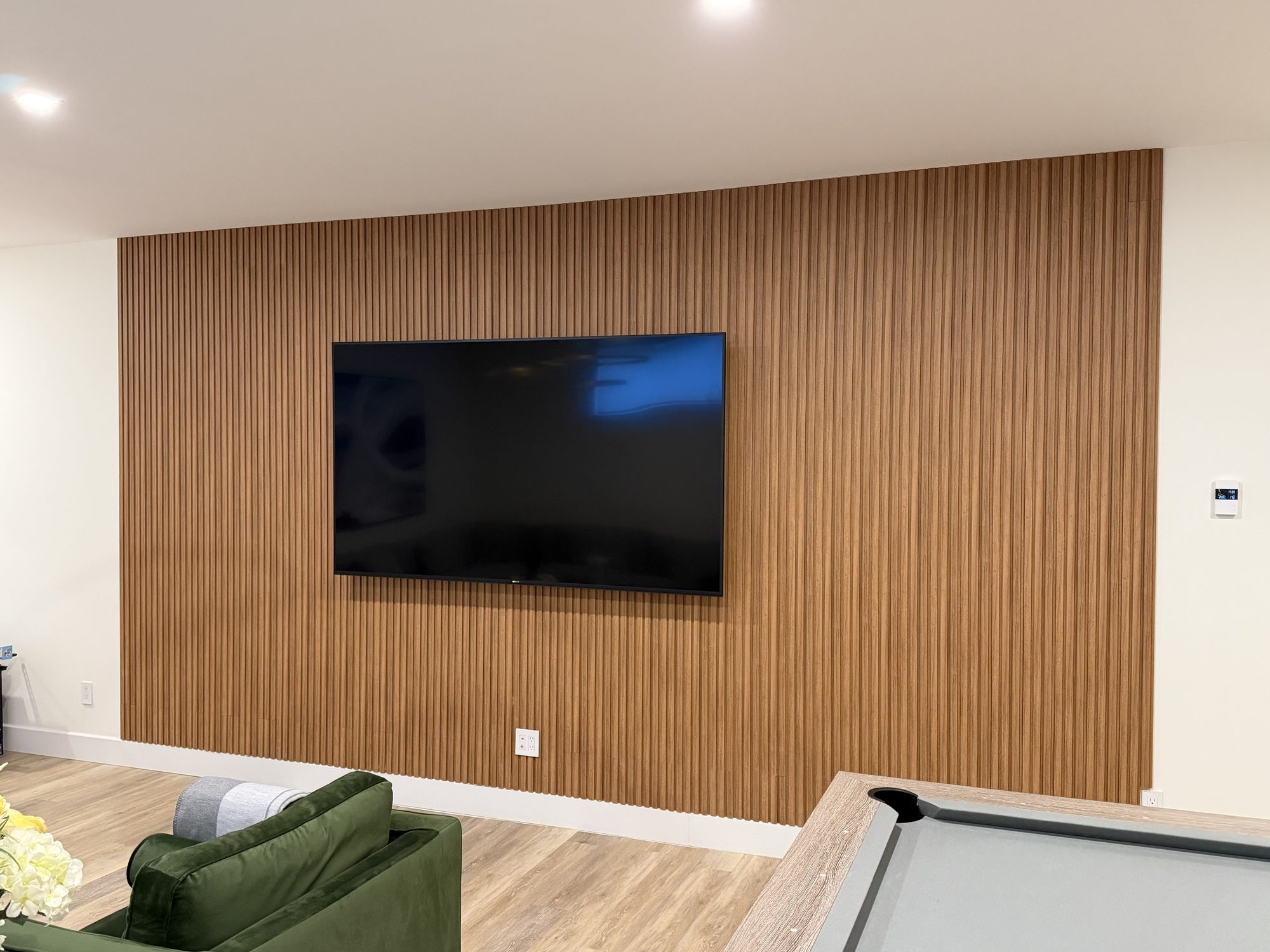Wall-mounted TV on a wood slat feature wall in a rec room with a pool table